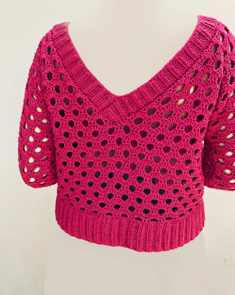 Back view of a deep pink crochet sweater with openwork holes, wide V-neck and ribbed hem displayed on a mannequin