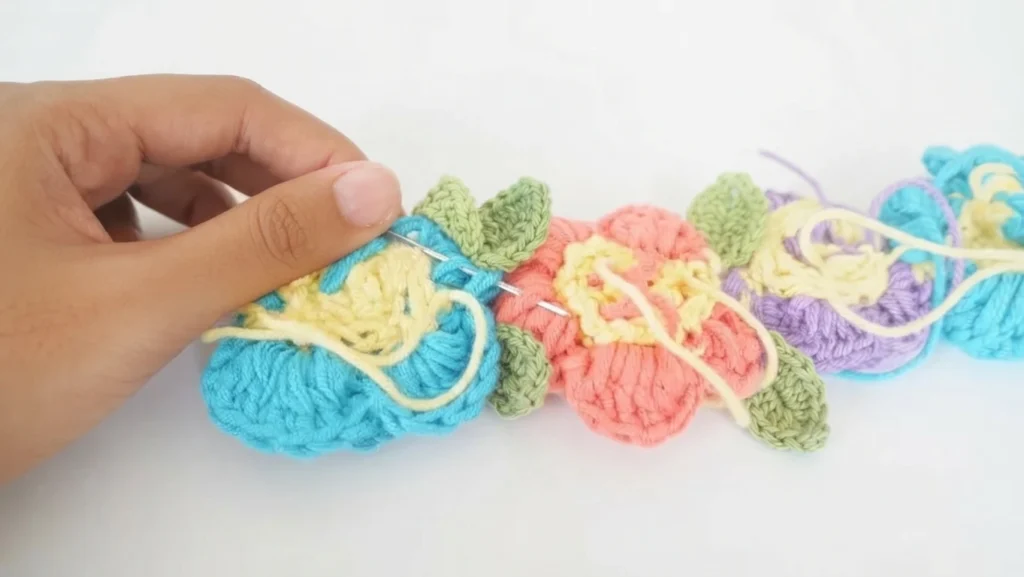Hand sewing colorful crochet flowers together with a yarn needle to form a flower crown