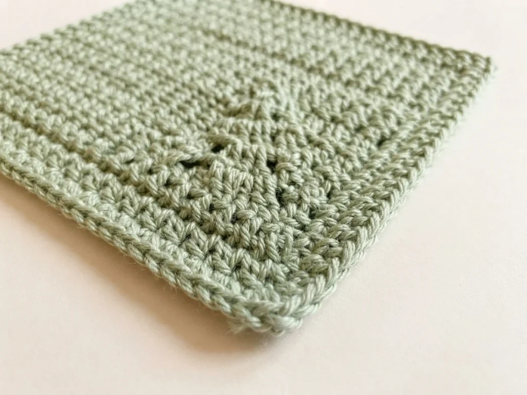 Close-up angled view of a light green crocheted square with openwork fir tree motif on a plain light background