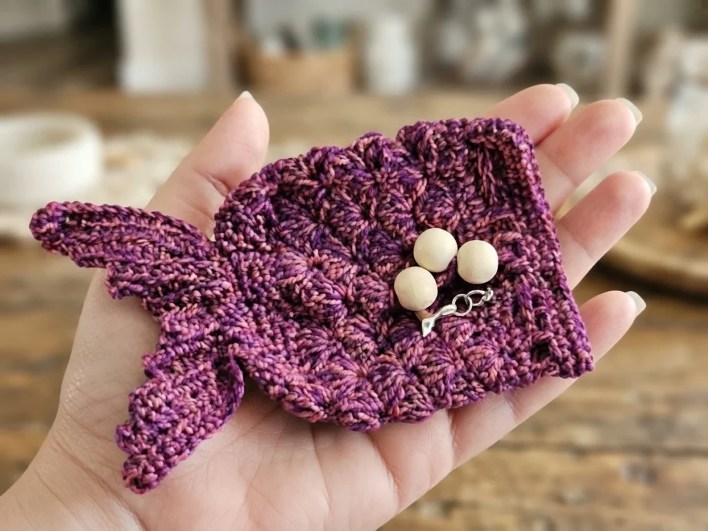 Hand holding a purple crocheted mermaid tail dice pouch with wooden beads and a small mermaid charm