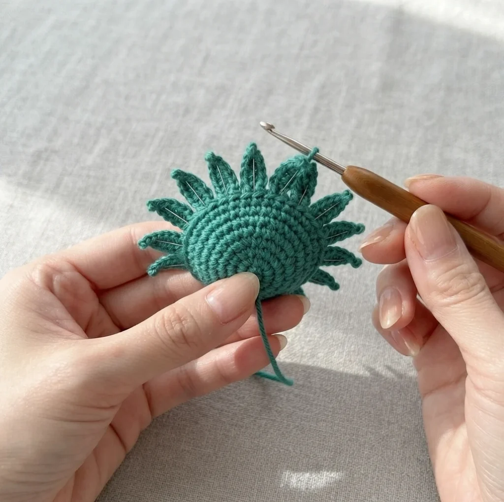 Hands holding a green crocheted flower base with pointed sepals around the edge and a crochet hook in the working loop