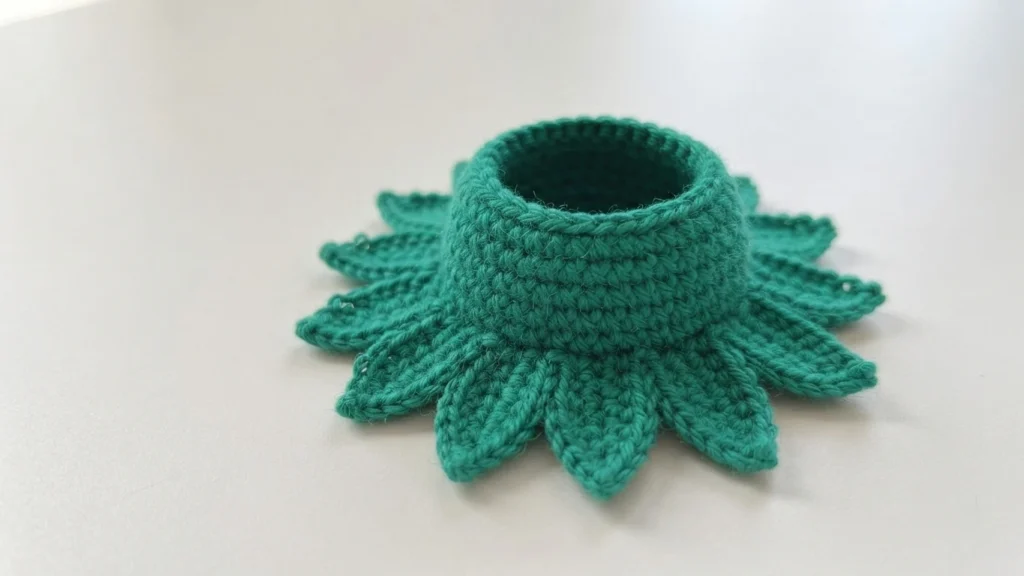 Green crocheted flower base with pointed sepals around a raised hollow center on a white surface