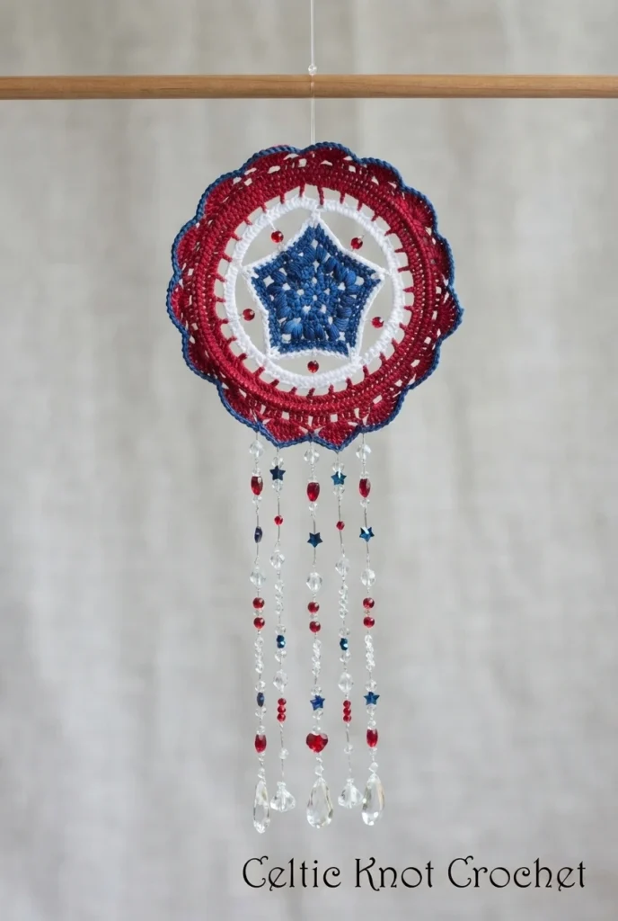 Red, white and blue crochet mandala with blue star center, white and red rings, and hanging beaded strands with clear teardrop beads, suspended from a wooden rod