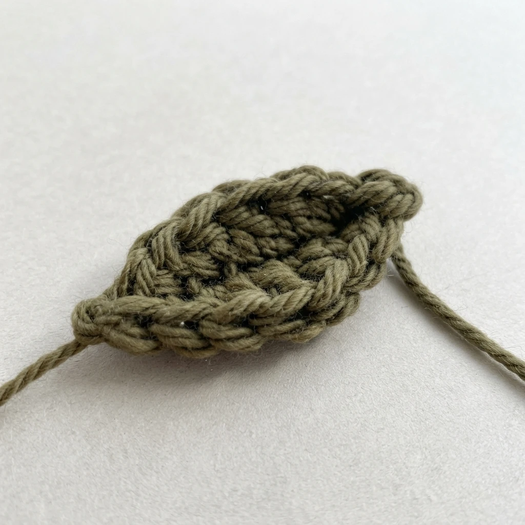 Close-up of a green crocheted leaf with yarn tails on a light background
