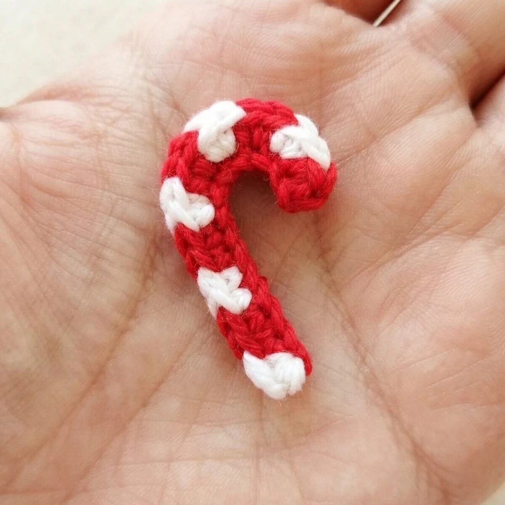 A small red-and-white crocheted candy cane resting on an open palm.