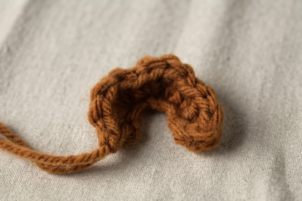 Small crocheted rust-brown piece with a long yarn tail, resting on gray woven fabric.