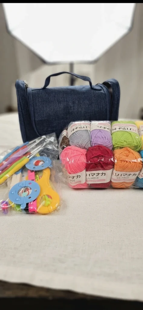 A blue crochet kit bag with colorful yarn skeins and crochet accessories arranged on a light-colored table.