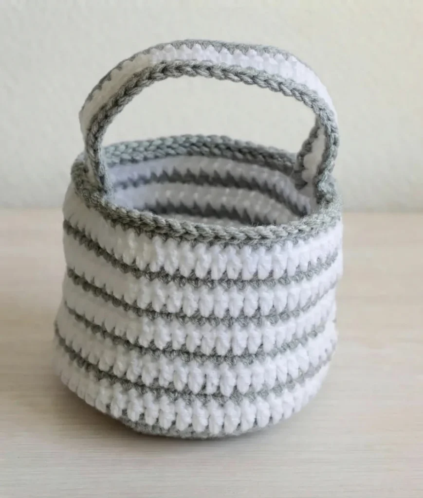 A white and gray striped crocheted bag with a gray-edged handle, shown without its mummy bandage or eyes.