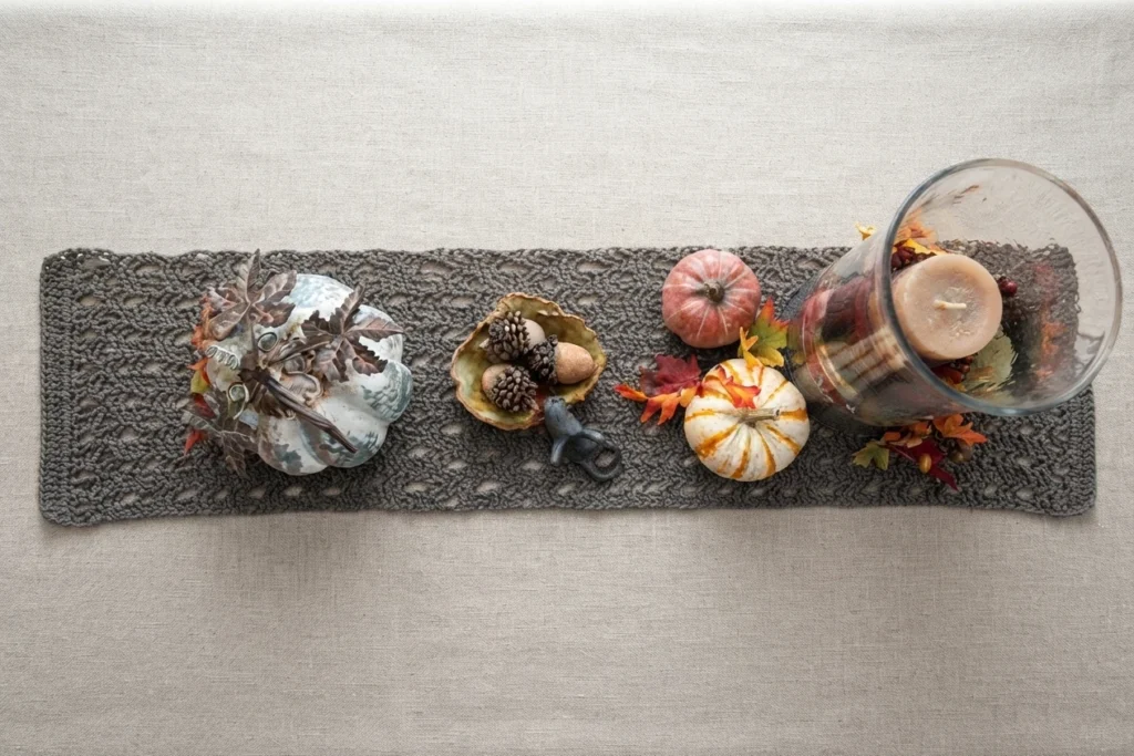 Chemin de table au crochet gris-brun décoré de citrouilles, de feuilles d’automne et d’un photophore en verre.