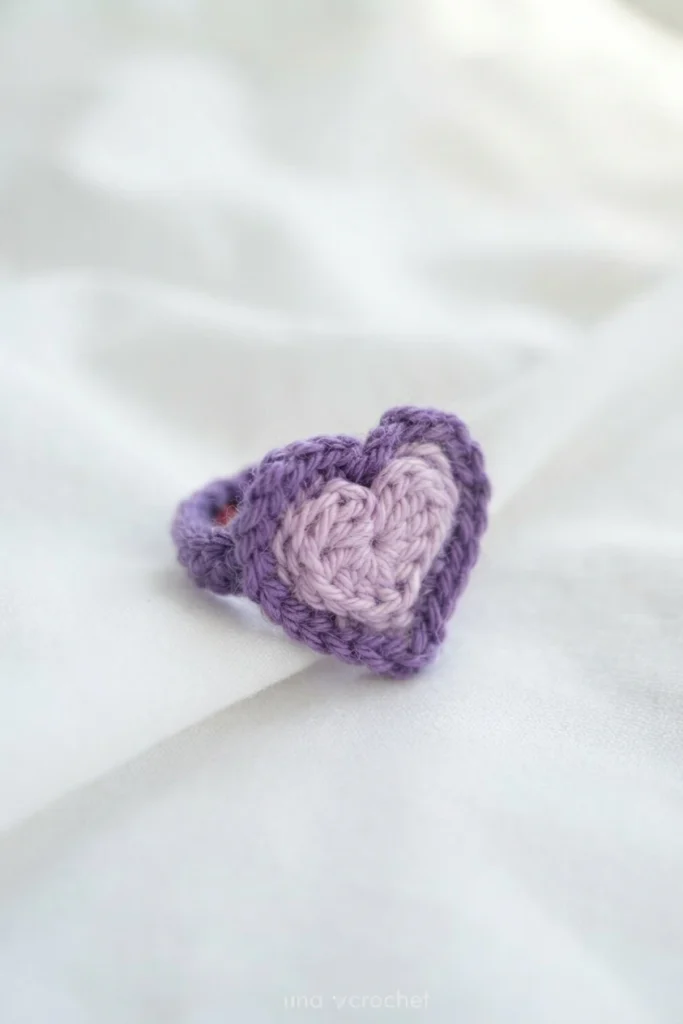 Crocheted heart ring with pale pink center and purple border on white fabric