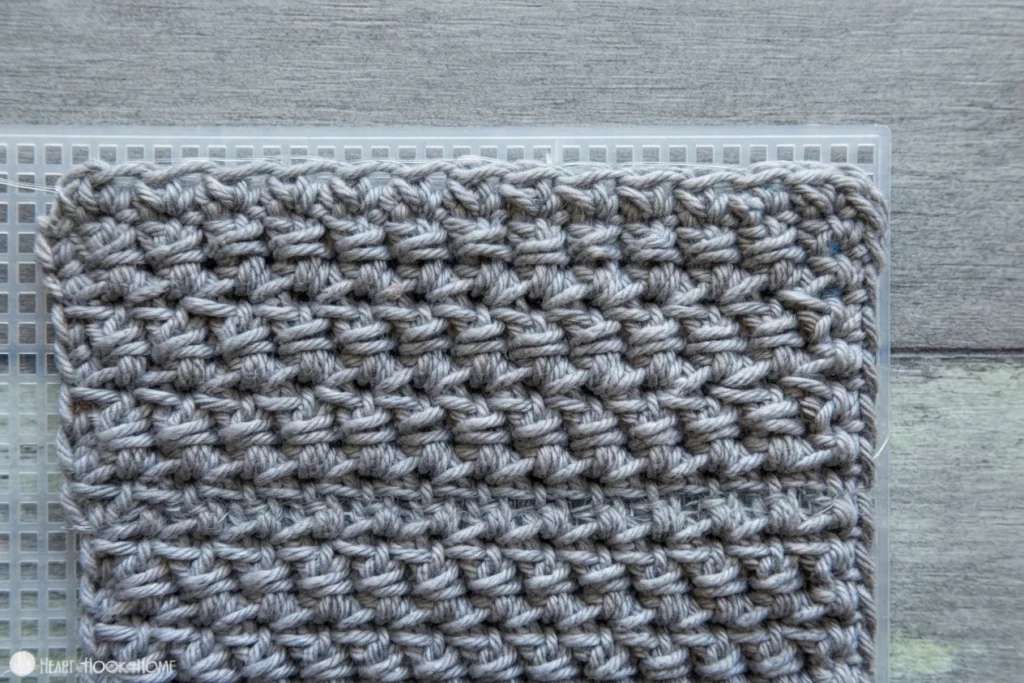 Panneau de crochet gris posé sur une toile plastique blanche, sur une surface en bois.