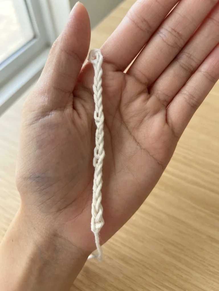White crochet chain held across an open palm above a light wooden surface