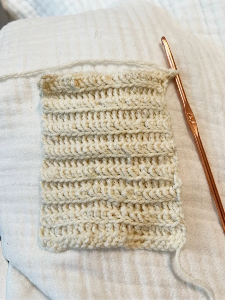 Cream half double crochet swatch with a copper crochet hook on white fabric