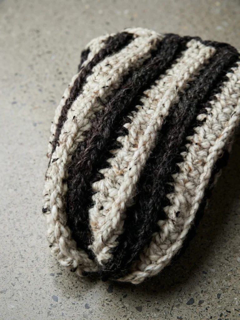 Tube crocheté rayé noir et crème, photographié debout sur une surface grise.