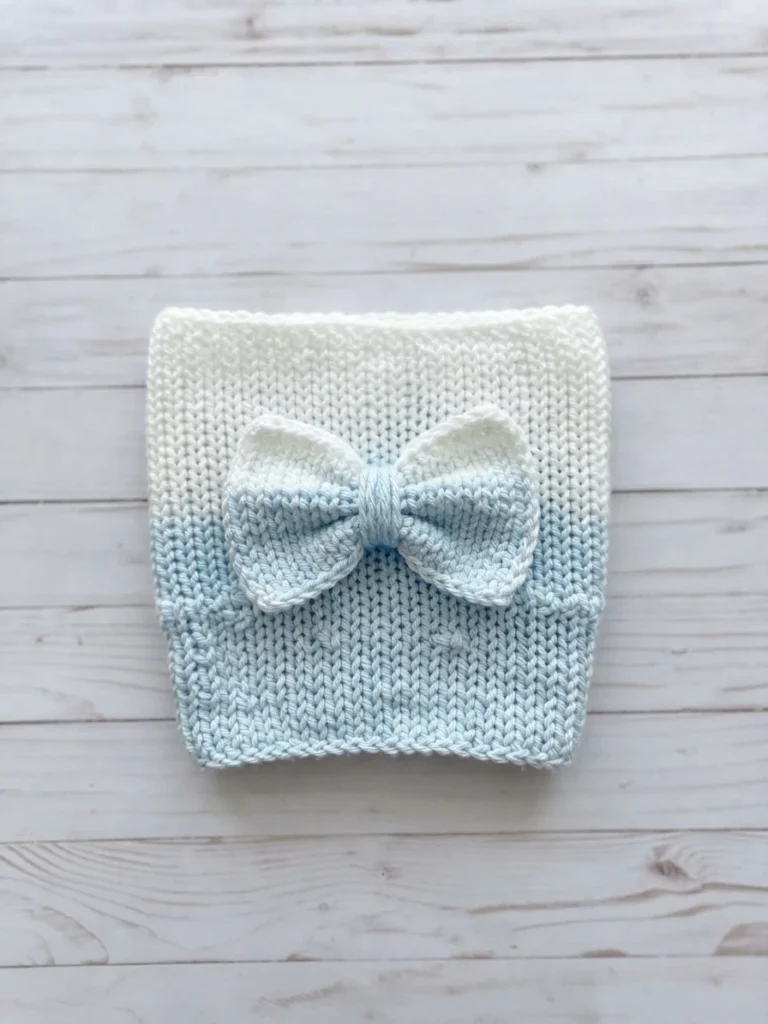 A flat blue-and-white crocheted cup sleeve with a matching bow on a pale wooden surface.