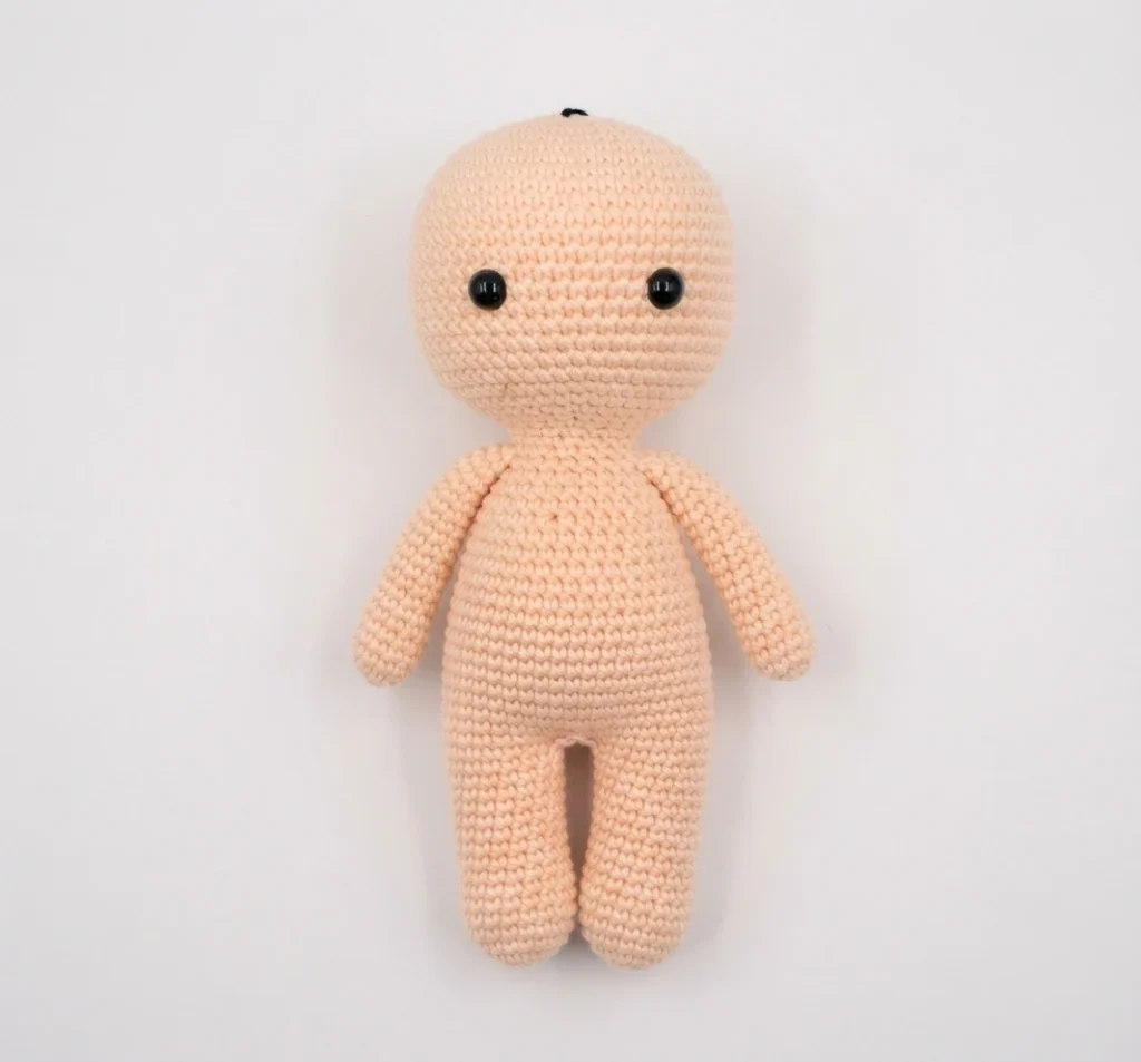 A small skin-colored crocheted amigurumi doll with black safety eyes, two arms and two legs, shown finished on a plain light background.