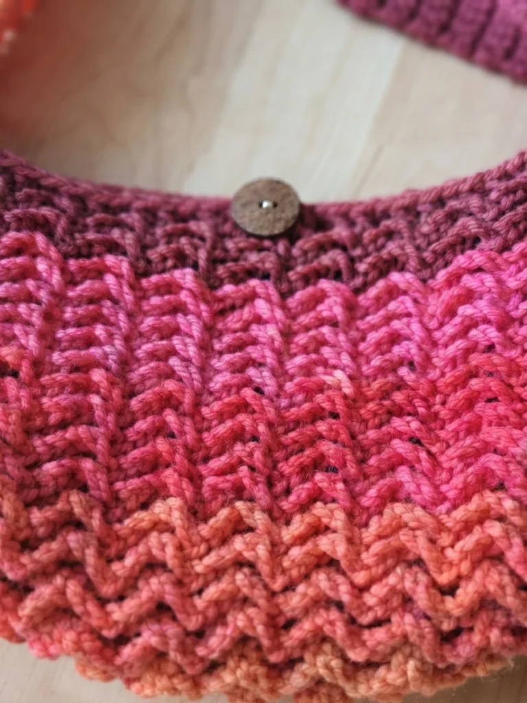 Close-up of a crocheted market bag in pink and orange self-striping yarn with a wooden button.