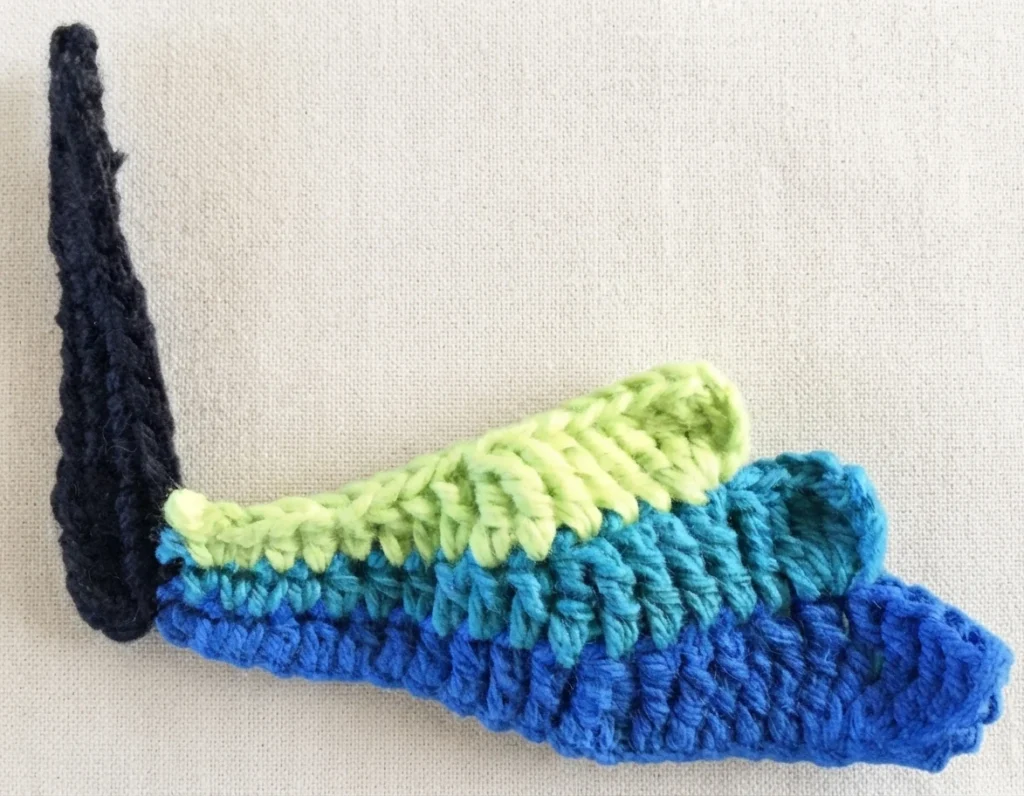 Close-up of a crochet butterfly's first wing section with blue, teal and green stripes joined to a black body.