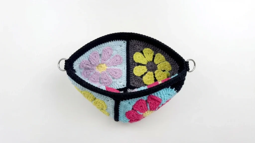 Top view of a crochet granny square bag opening with a black border, floral motifs, and two metal rings