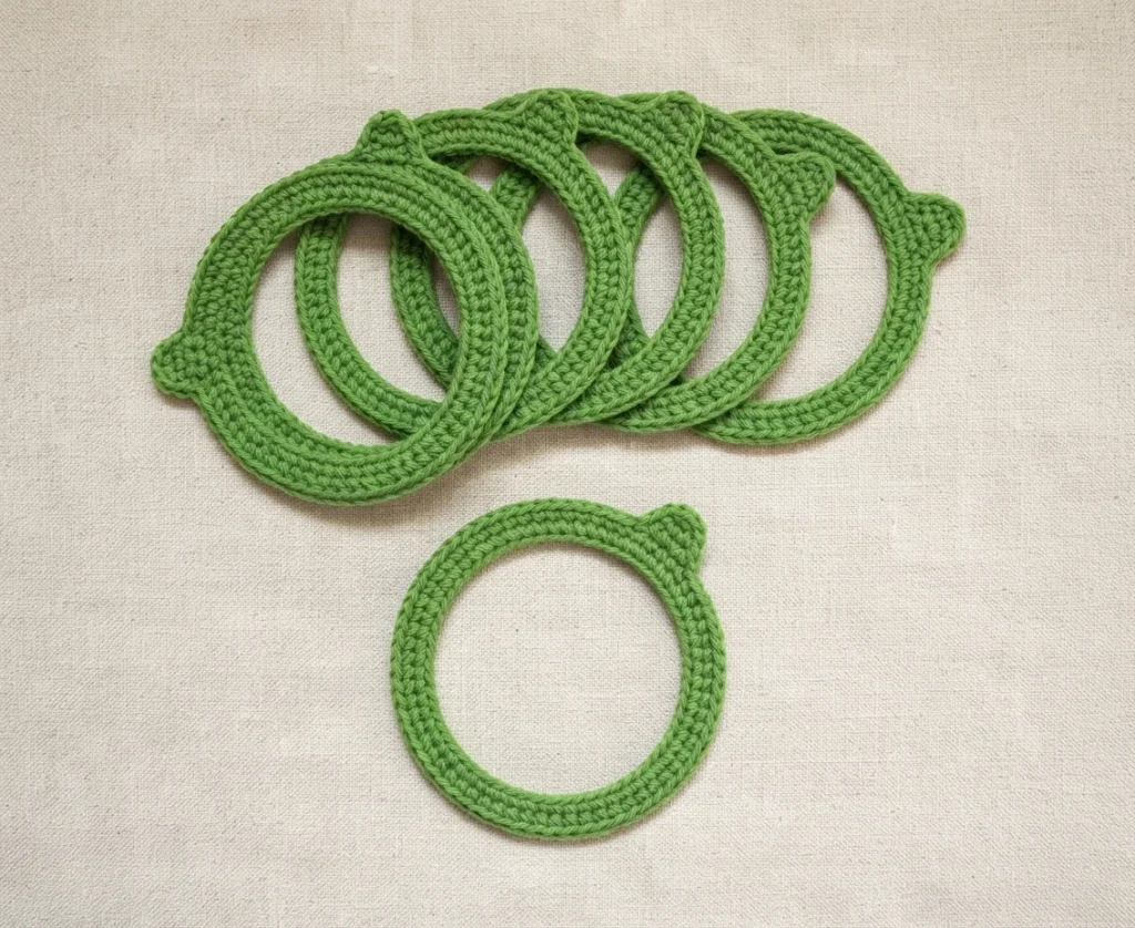 Several green crocheted rings overlap on a beige surface, with one separate ring below.