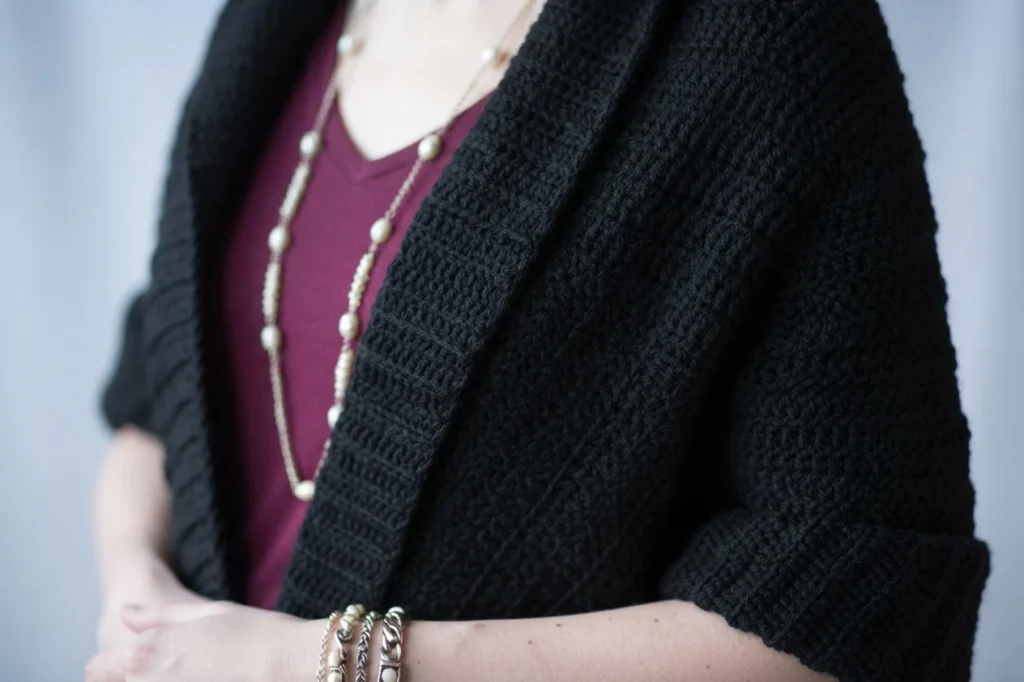 Close-up of a black crocheted shawl worn over a burgundy top, with a beaded necklace and bracelets.