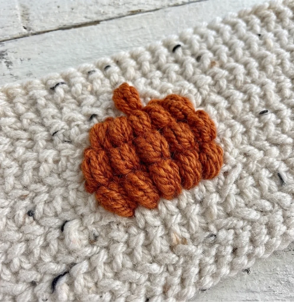 Close-up of a raised orange crochet motif on speckled ivory fabric.