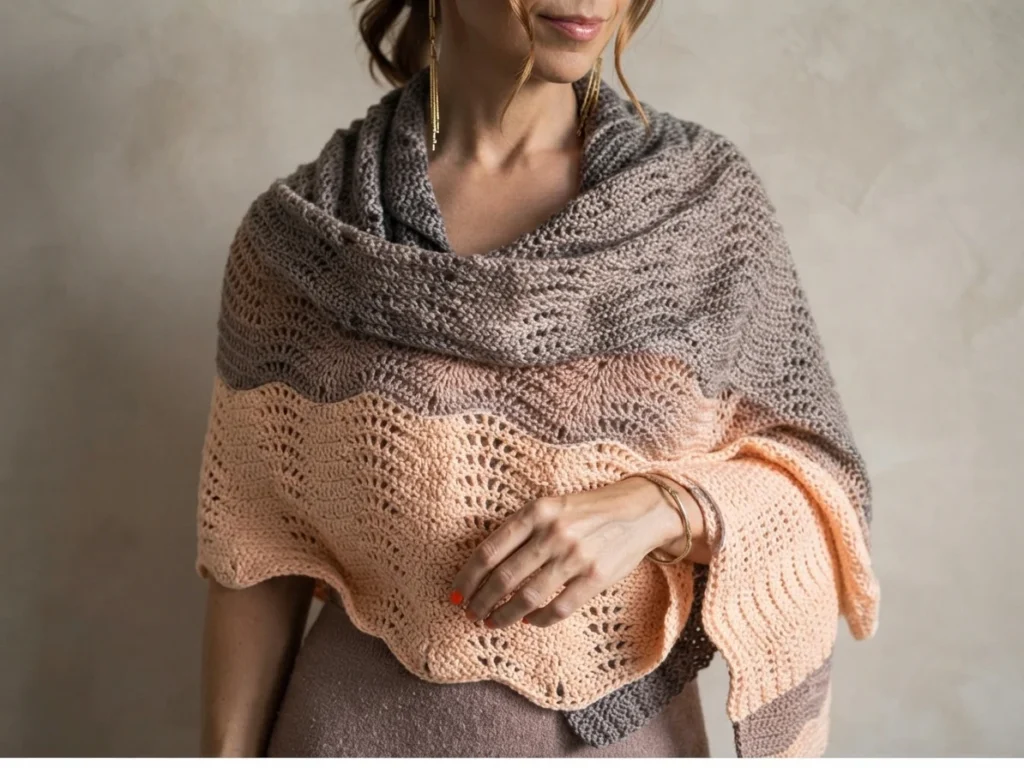 Une femme porte un châle au crochet ondulé gris et pêche, drapé sur ses épaules.