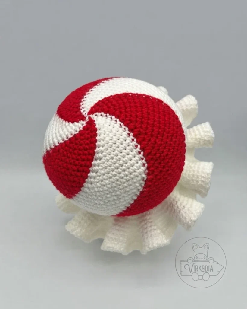 Top view of a crocheted red-and-white peppermint hat with spiral color sections and a white ruffled edge.