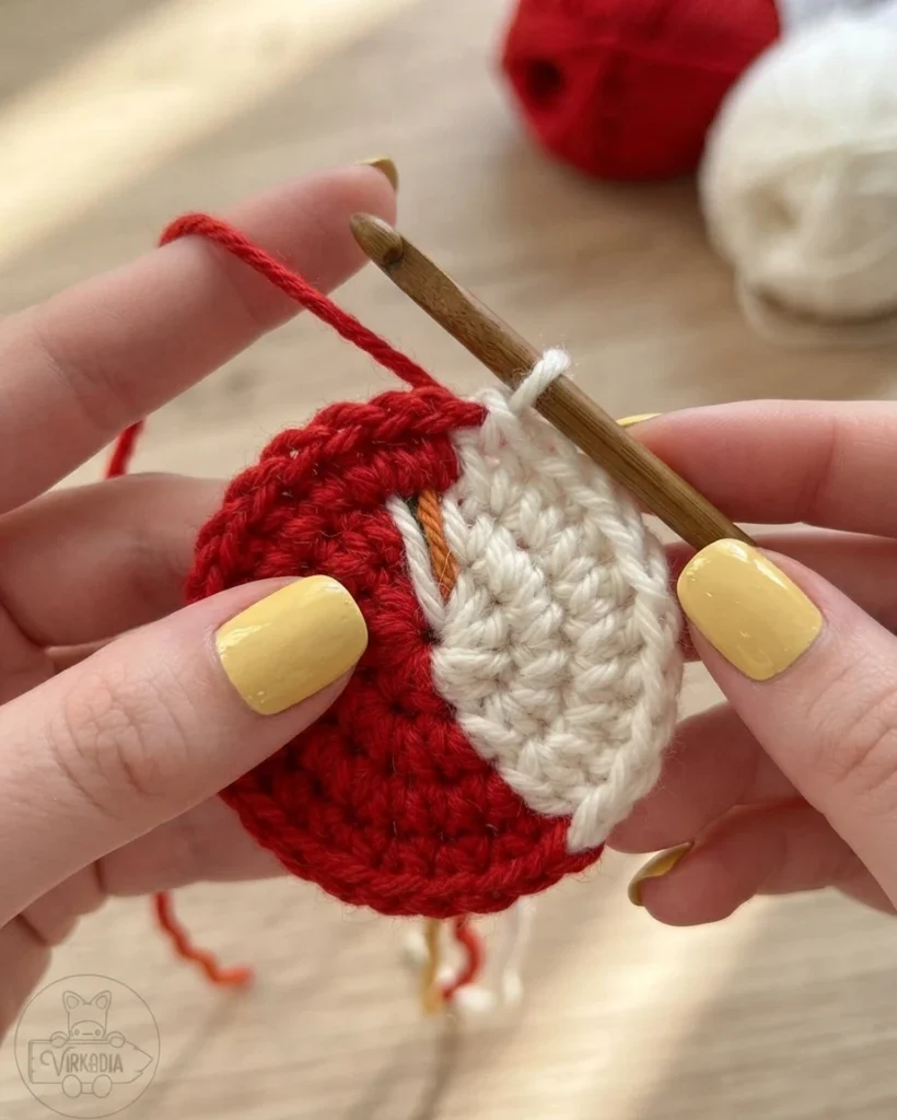 Hands crochet a small red-and-white circular piece, switching yarn colors at the boundary with a hook.