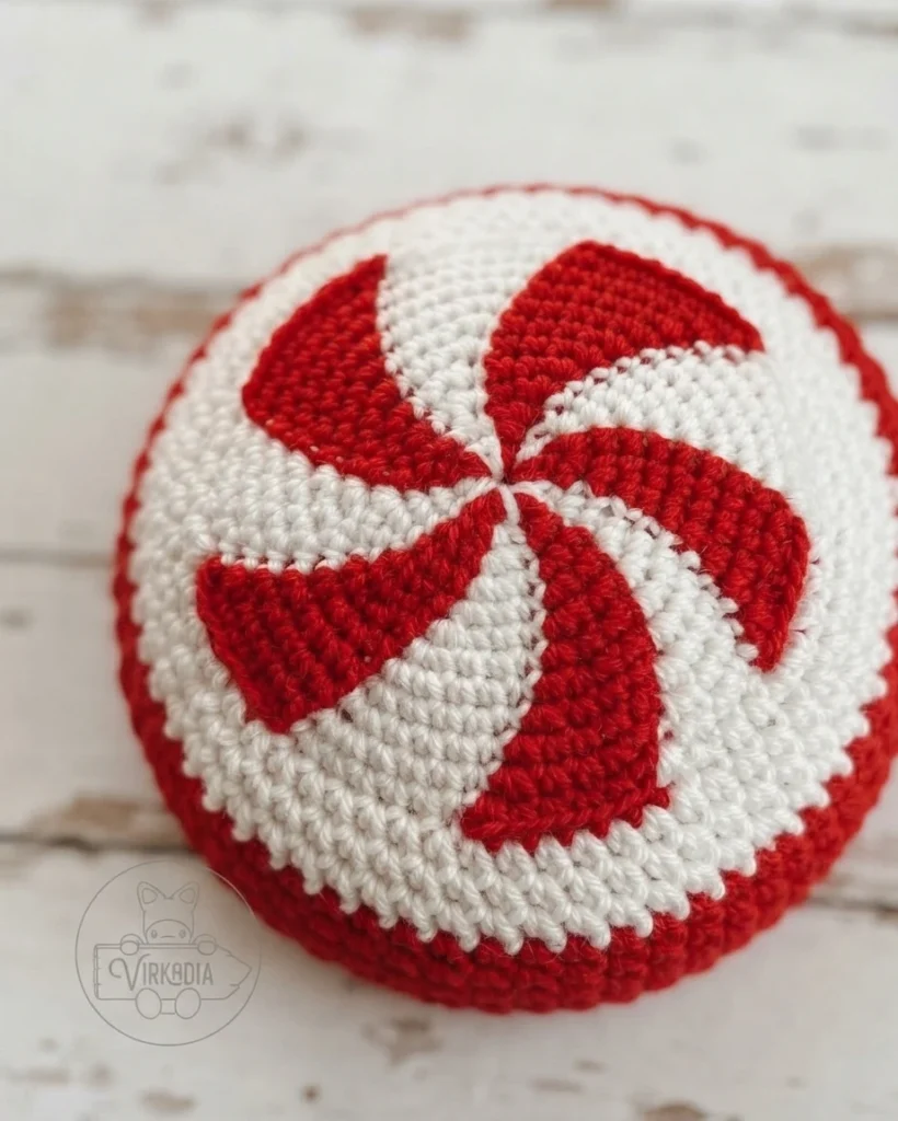 Close-up of a crocheted red-and-white peppermint spiral crown in progress.