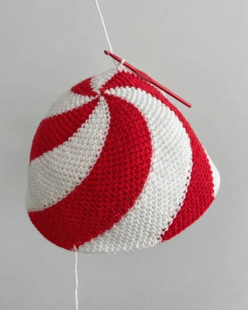 Un bonnet crocheté rouge et blanc en forme de dôme, avec un crochet rouge près du sommet.