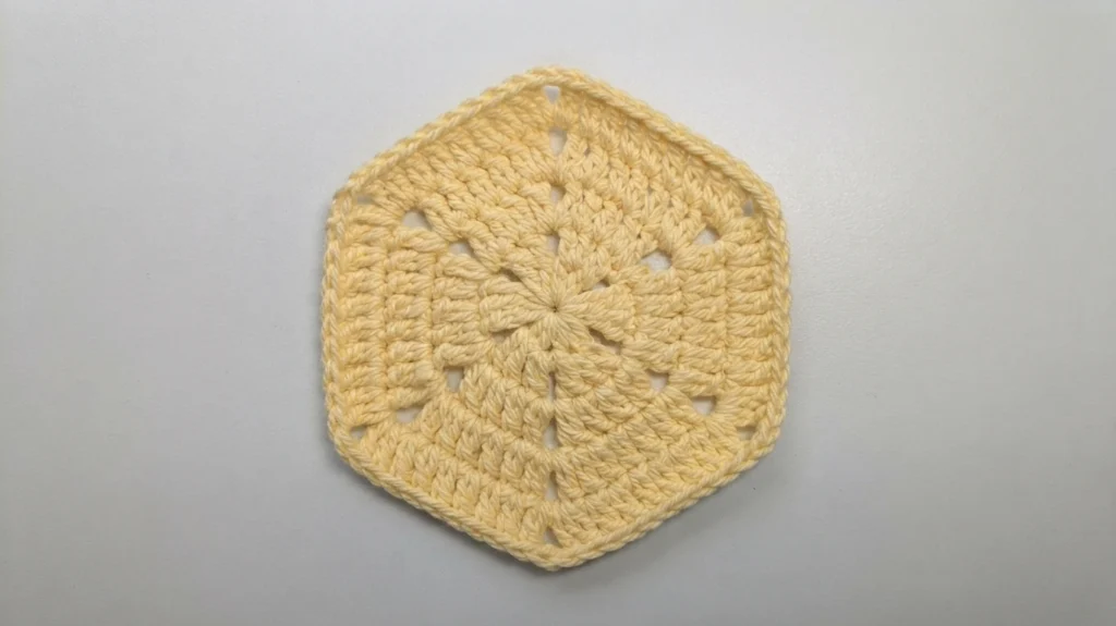 Close-up of a single pale yellow crochet hexagon with openwork details on a white surface