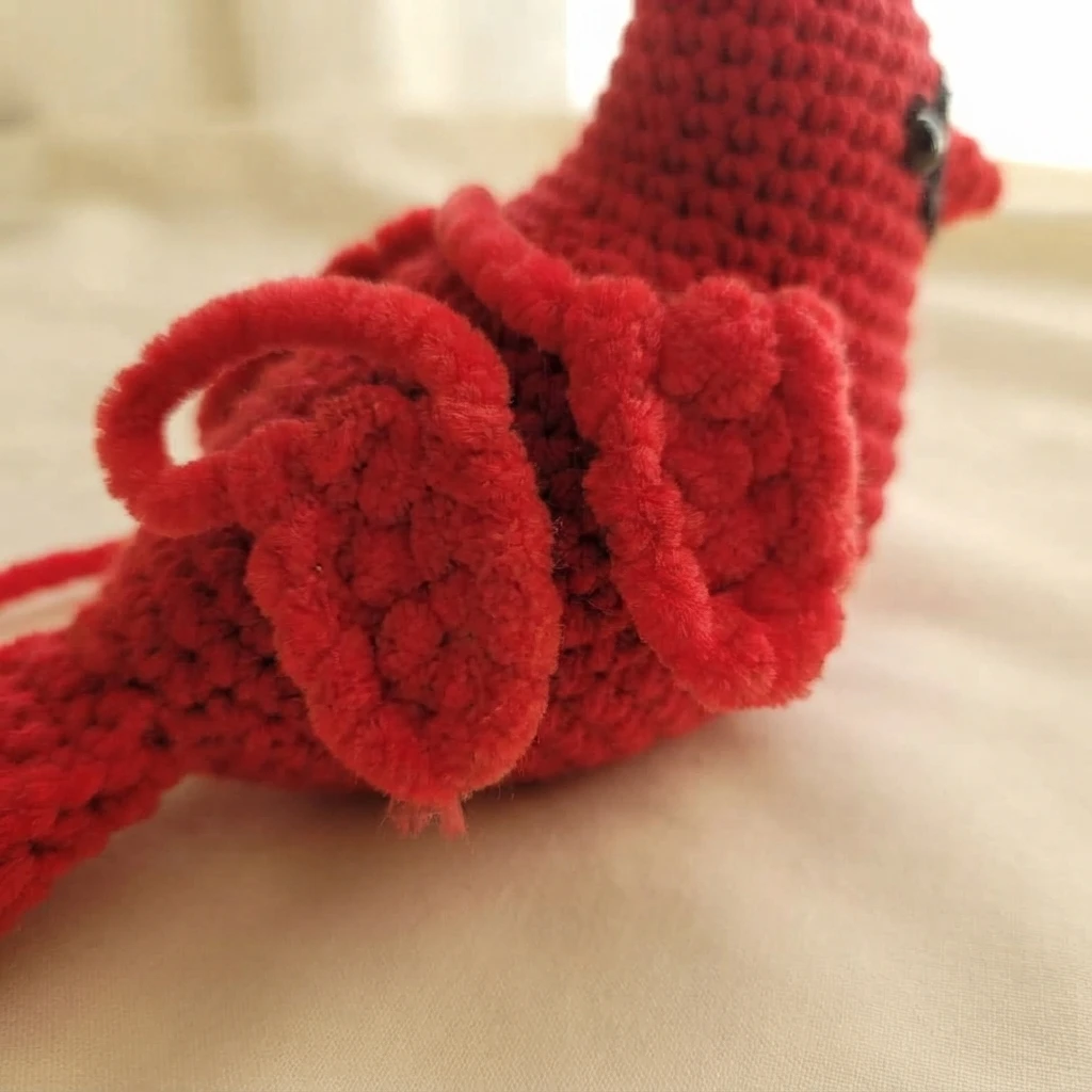 Gros plan d’un cardinal au crochet rouge, avec une aile rouge attachée et une partie de son œil visible.