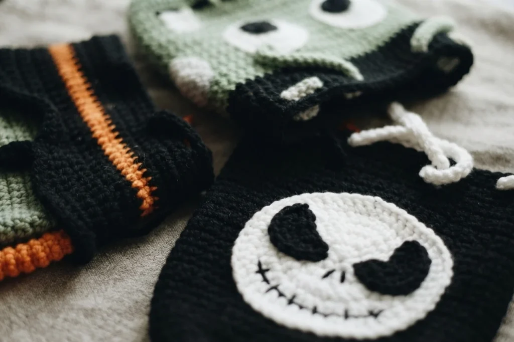 Close-up of a crocheted black bag with a white skull face, beside parts of green and black Halloween bags.