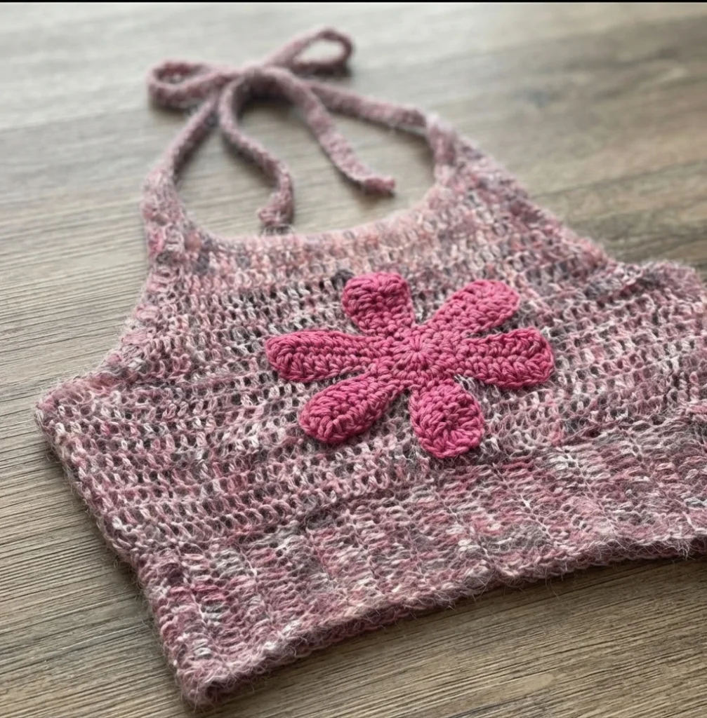 Crocheted pink halter top with a large magenta flower applique, laid flat on a wooden surface