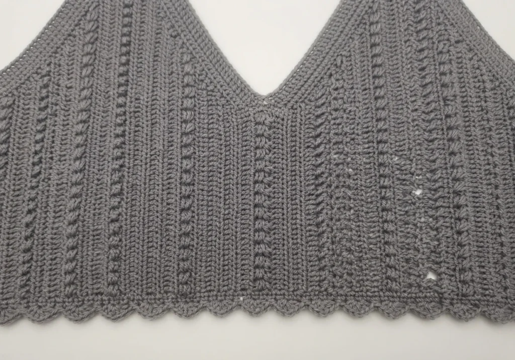 Close-up of the bottom edge of a gray crocheted V-neck summer top, showing a scalloped picot trim along the hem.