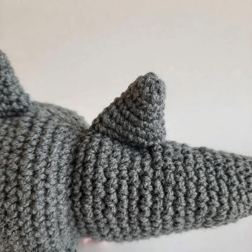 Close-up of a small gray crocheted back fin sewn onto the back of a gray and white crocheted shark possum plush near the base of the tail.